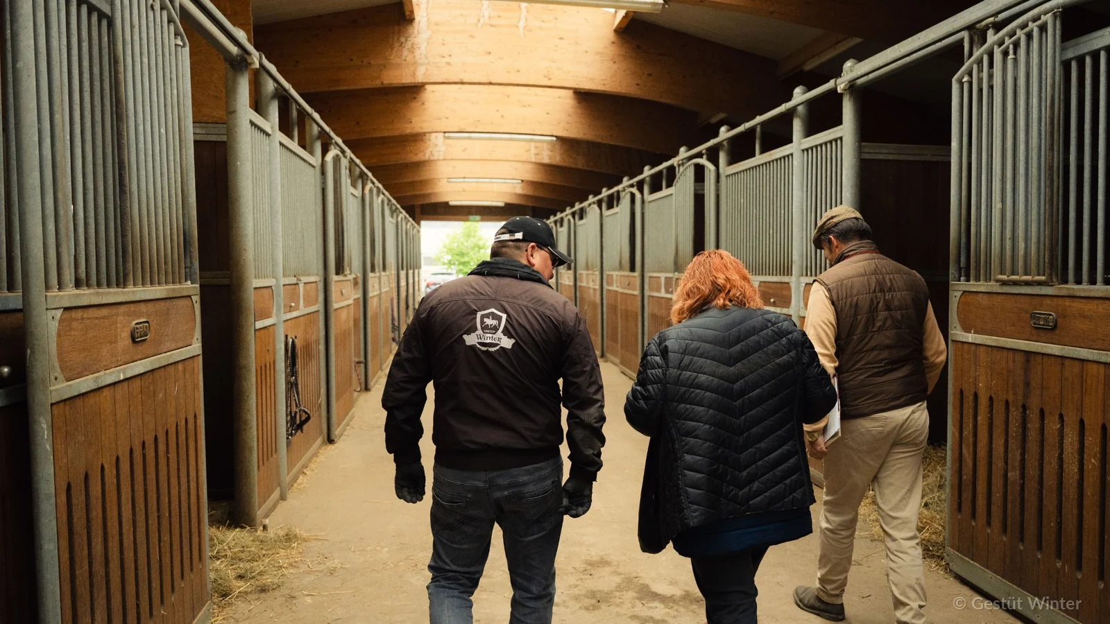 Three people walking through the stable aisle at Gestüt Winter